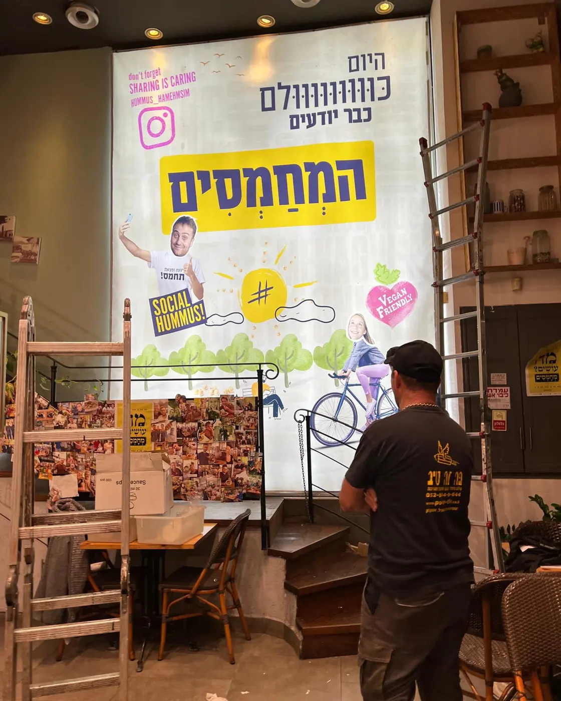 חנן מול הדפסת קיר גדולה שהתקין, בחולצת פה זה טיב